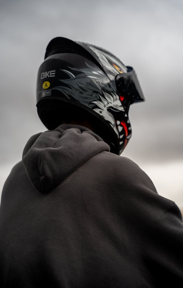 Rear view of motorcyclist wearing helmet, looking at cloudy sky, evoking a sense of adventure.