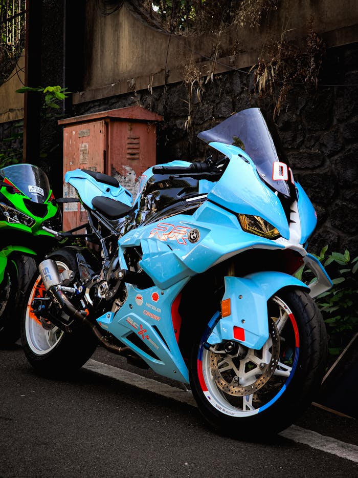 Photo of a blue sports motorcycle with racing decals parked next to a green bike on an urban street.